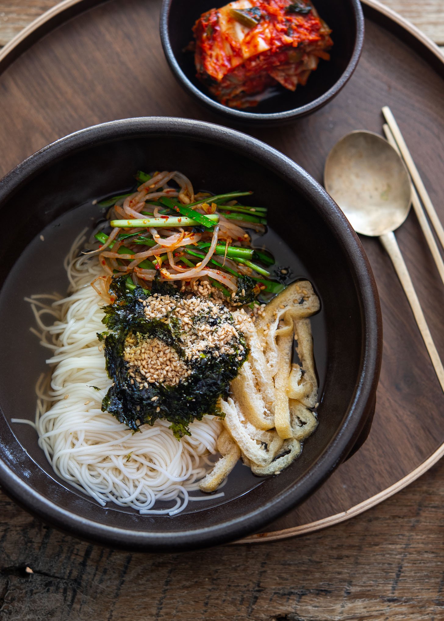 Janchi guksu noodle soup with somyeon, tofu, mung bean sprouts, and chives in a light broth.